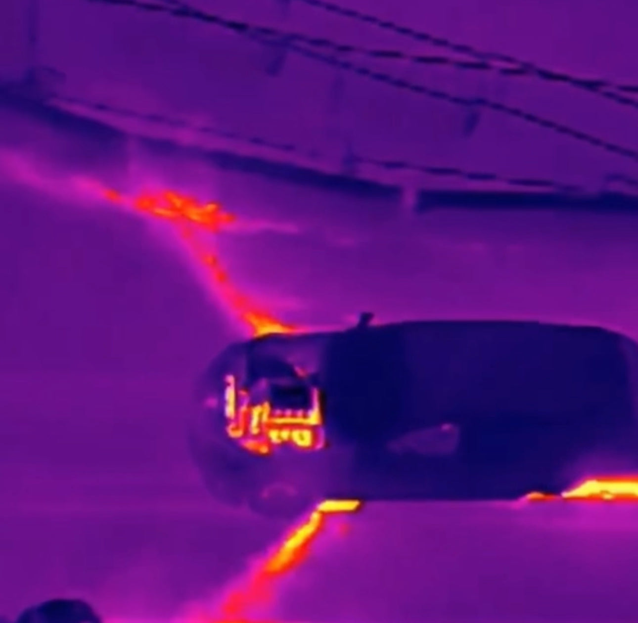 Thermal imaging of a car on a road with visible heat signatures.